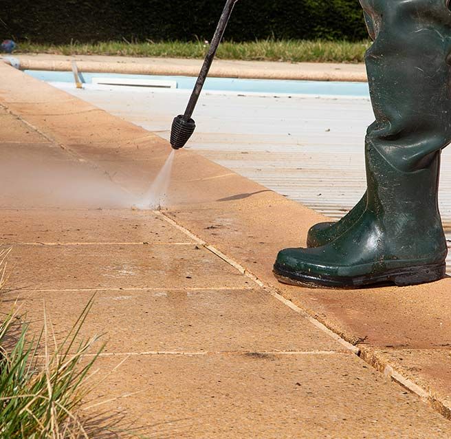 Personne bottée en gros plan nettoyant à haute pression les abords d’une piscine