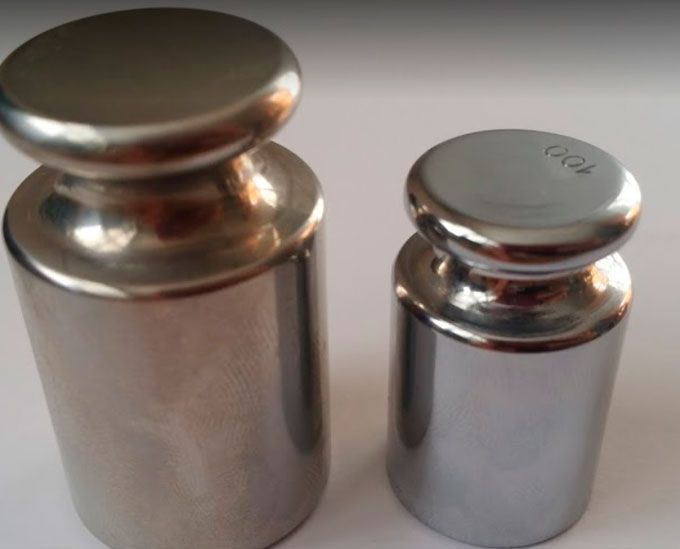 Dos pesas de acero inoxidable están una al lado de la otra sobre una superficie blanca.