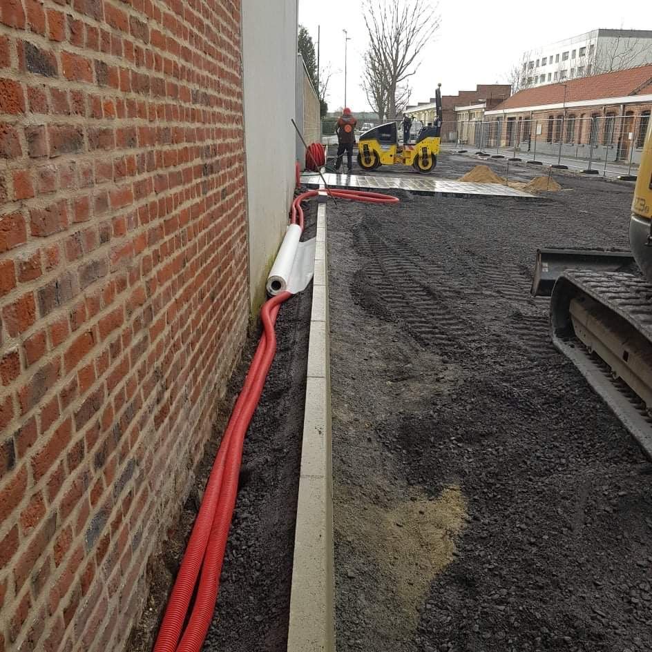 Travaux de sol d'un extérieur de maison avec la pose de tuyaux contre un mur