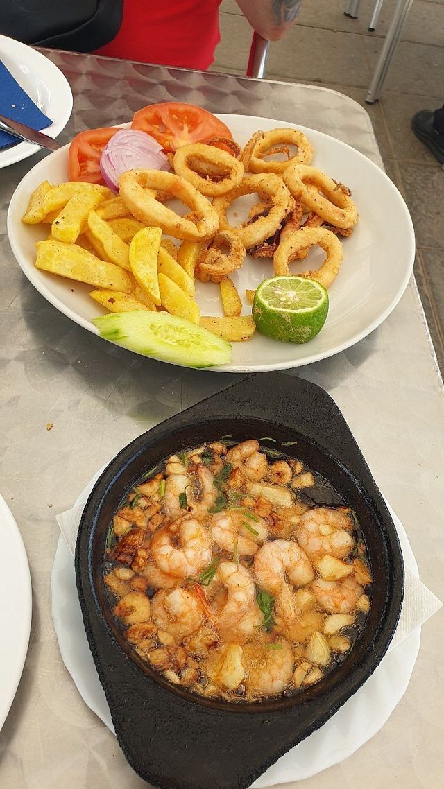 Plato de calamares fritos y patatas fritas, y un plato de camarones al ajillo.
