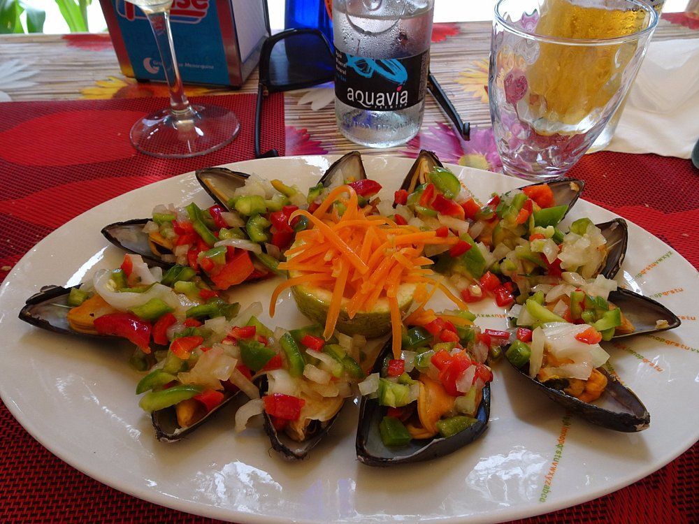 Plato de mejillones con verduras en cubos, lima y zanahoria rallada. Mesa con bebidas.