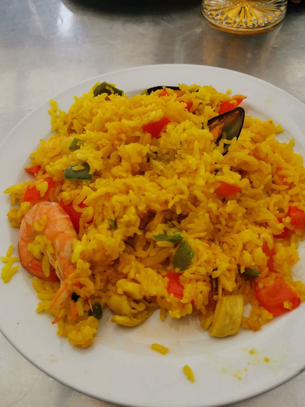 Paella con camarones, mejillones y verduras en un plato blanco.