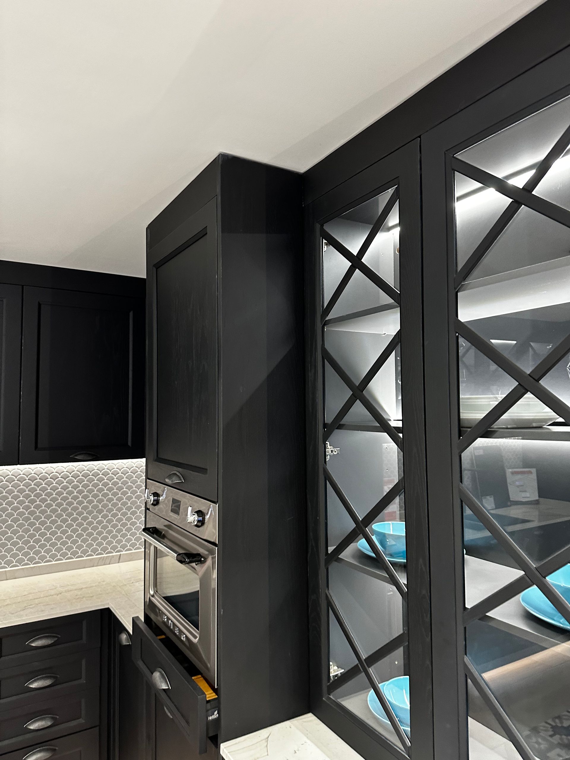 Muebles de cocina negros con horno incorporado, uno de ellos con vitrina revestida de vidrio e iluminación interna.