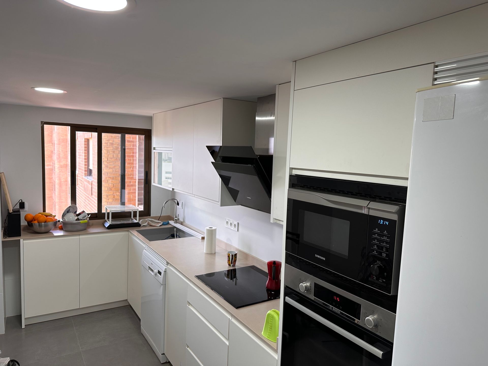 Cocina blanca moderna con electrodomésticos de acero inoxidable, anafe y ventana.