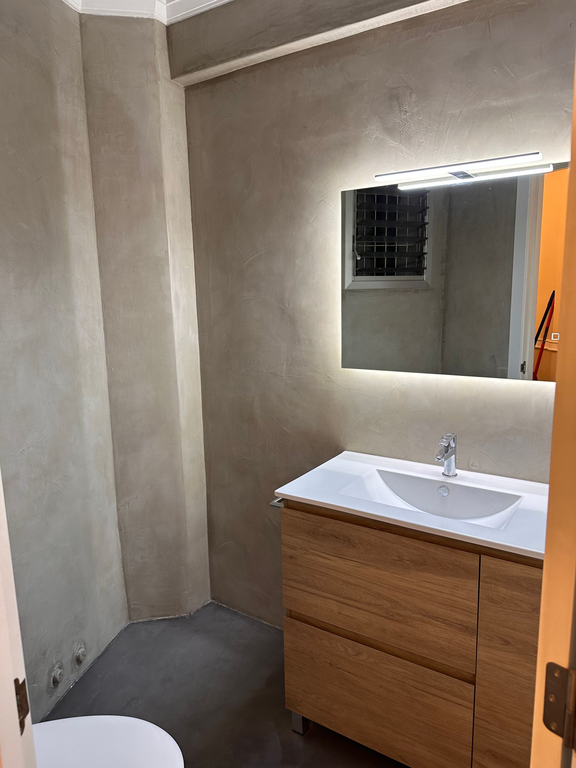 Baño moderno con tocador de madera, espejo grande y paredes grises.