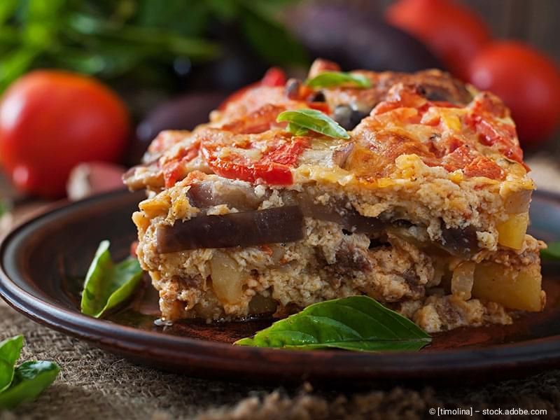 Ein Stück Gemüseauflauf mit Auberginen, Tomaten und Kräutern auf einem dunklen Keramikteller.