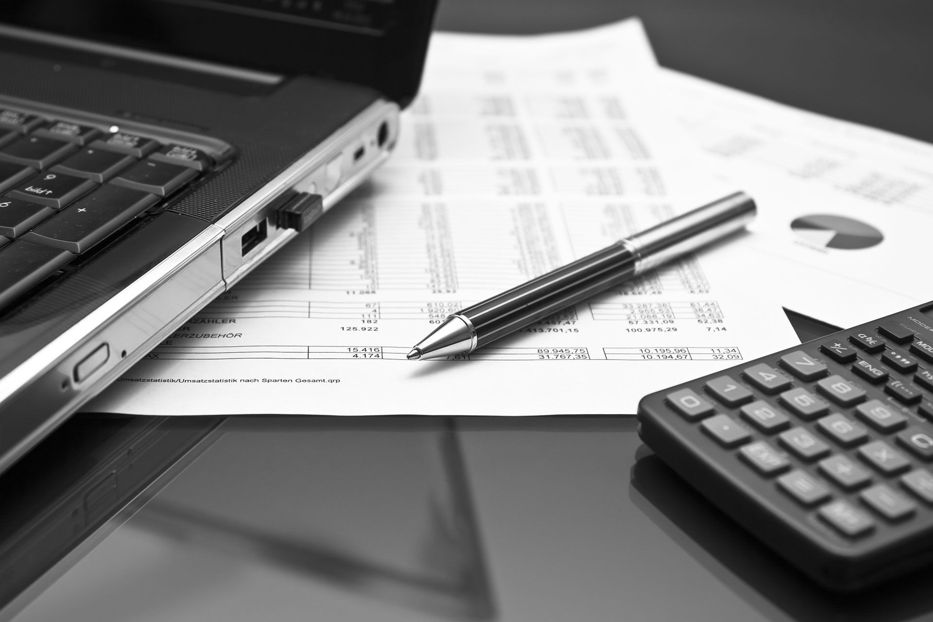 Ein Stift liegt auf einem Blatt Papier neben einem Laptop und einem Taschenrechner.