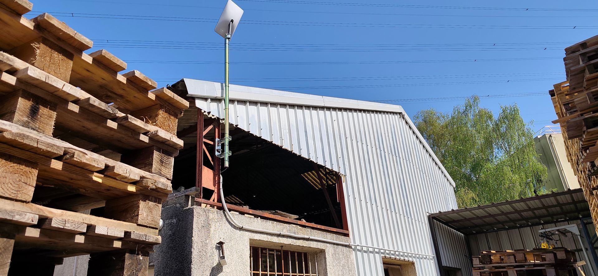 Bâtiment industriel au toit métallique incurvé, à côté de palettes en bois empilées sous un ciel bleu.