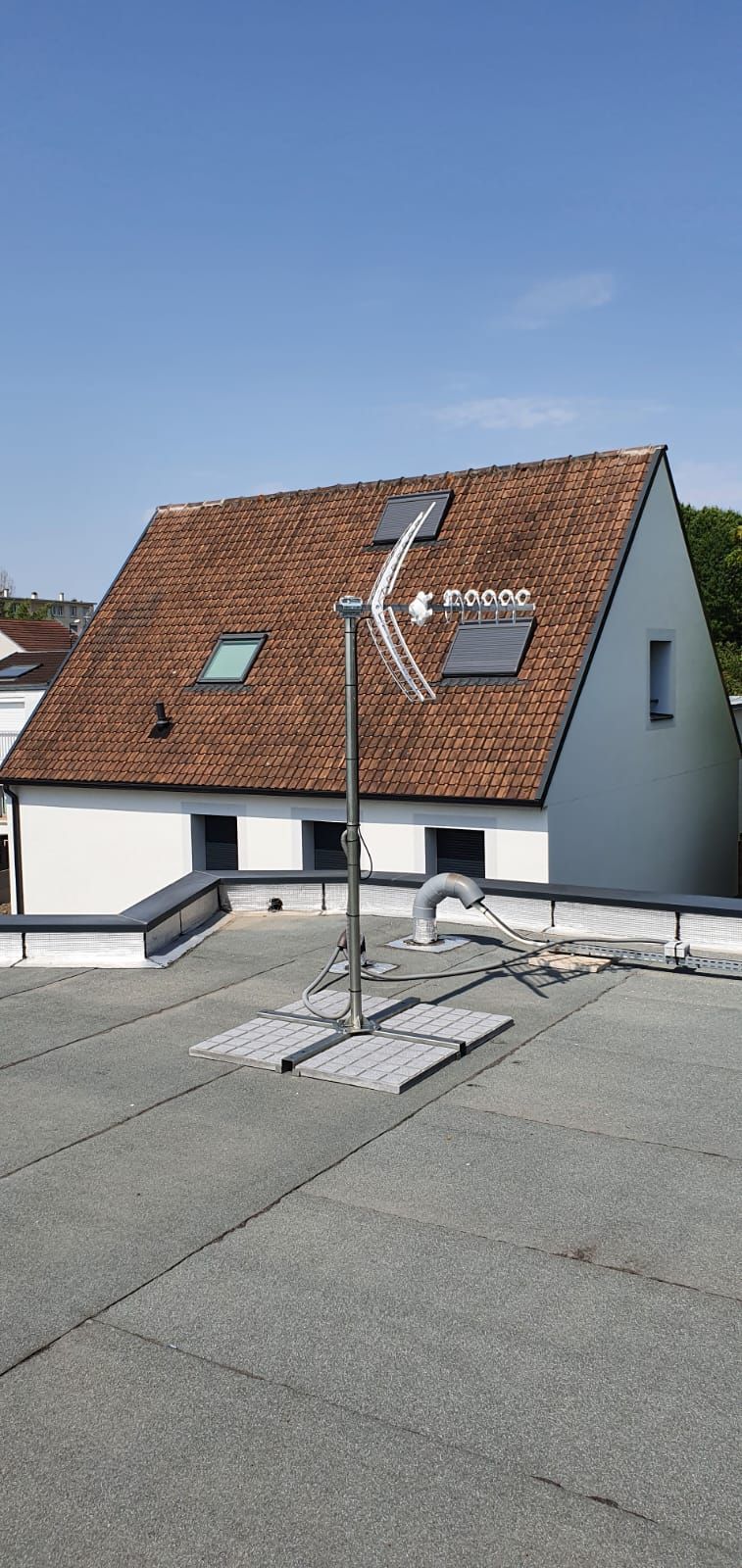 Panneau solaire sur le toit d'une maison aux tuiles rouges avec cheminée et puits de lumière sous un ciel dégagé