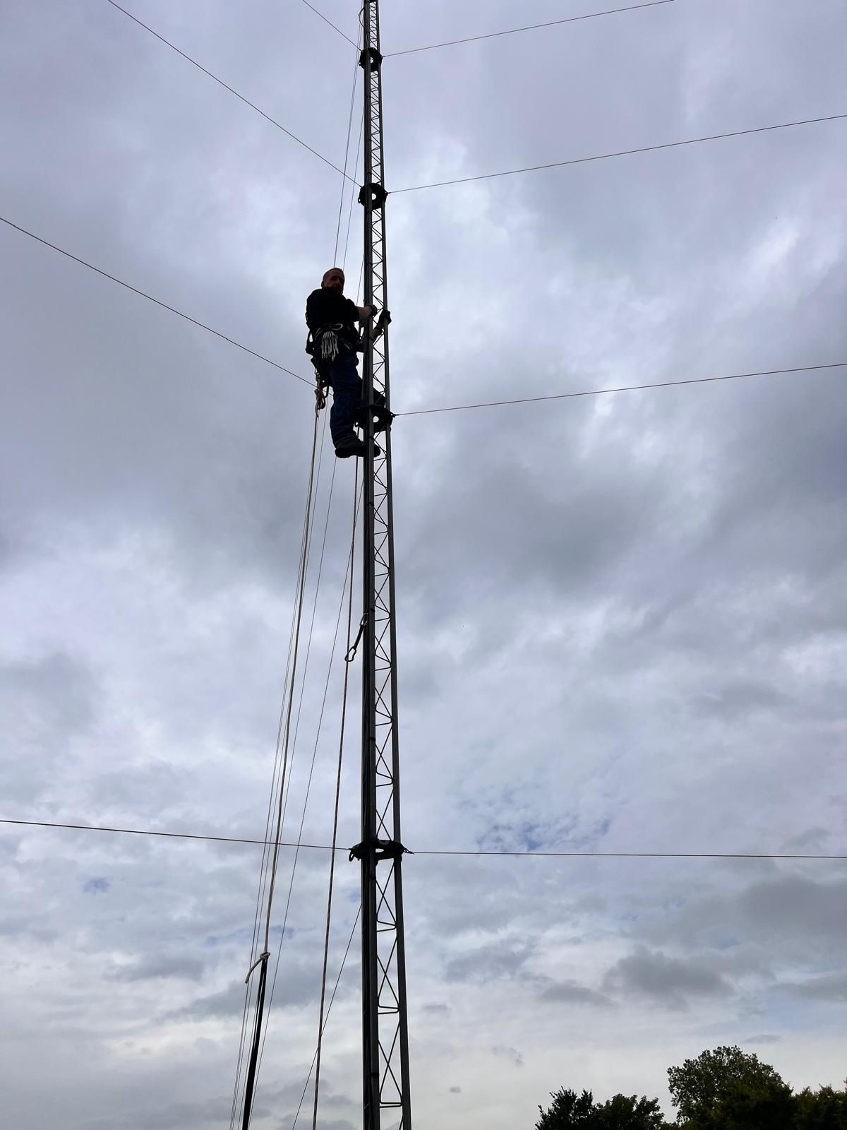 Personne escaladant une haute tour radio sur fond de ciel nuageux
