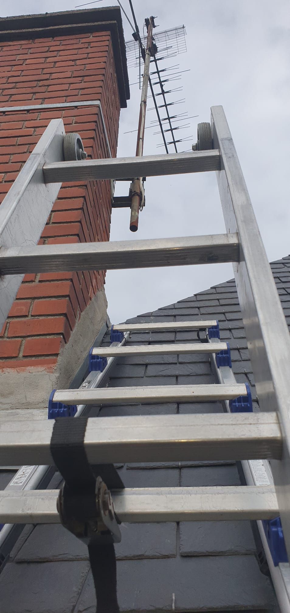 Des échelles appuyées contre un bâtiment en briques, sur un mur extérieur, avec un échafaudage métallique au-dessus.
