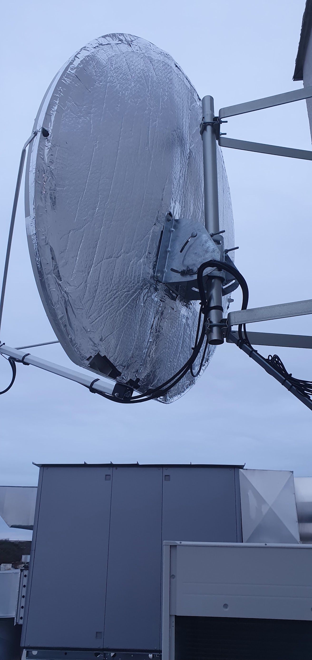 Une grande antenne parabolique recouverte de neige sur un toit, se détachant sur un ciel d'hiver gris.
