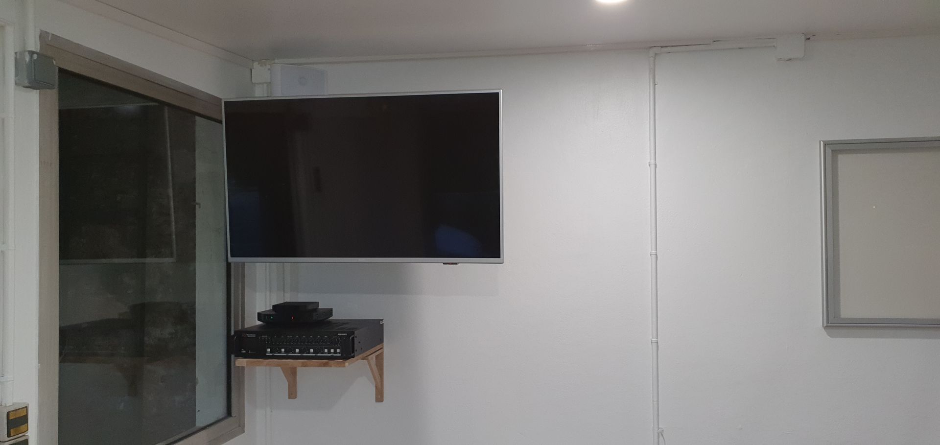 Pièce minimaliste avec télévision murale, petite étagère, fenêtre et porte sur murs blancs