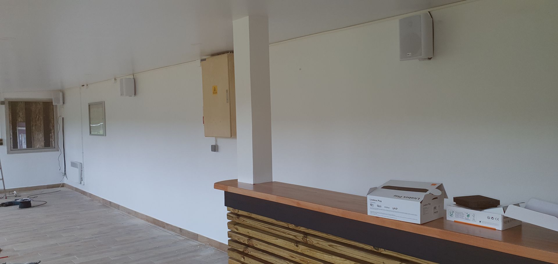 Pièce lumineuse et vide, aux murs blancs, avec des haut-parleurs muraux et un comptoir avec une imprimante.