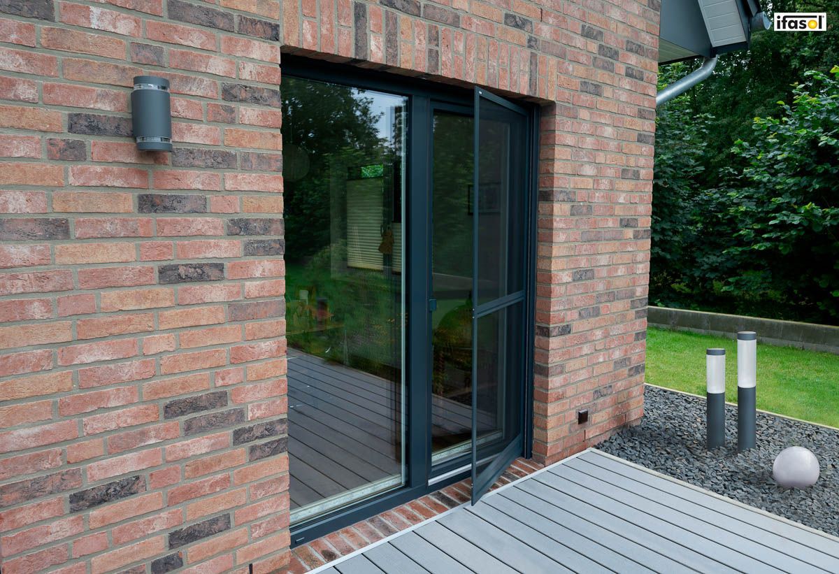 ein Backsteingebäude mit einer Schiebetür und einem Holzdeck - Insektenschutz von Gardinen Breuß aus Elmshorn