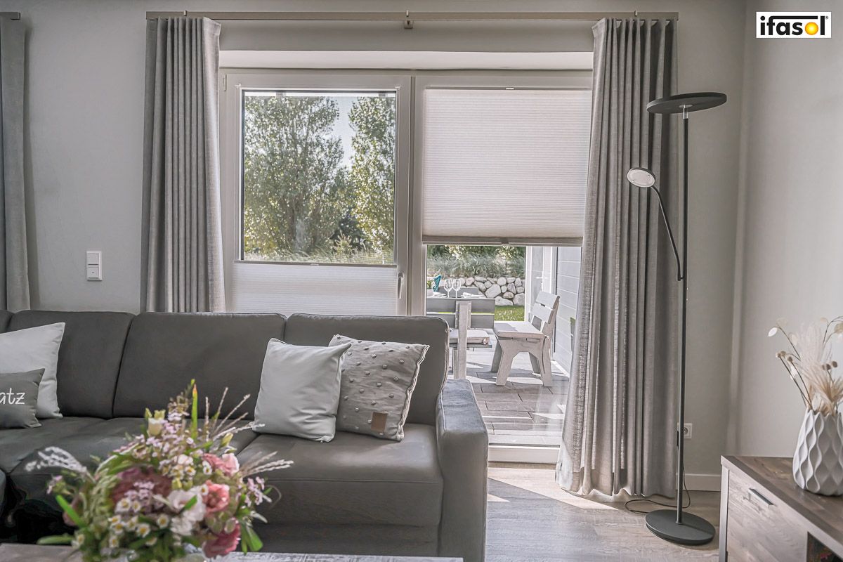 ein Wohnzimmer mit einer Couch , einem Tisch und einem Fenster - Sonnenschutz von Gardinen Breuß aus Elmshorn