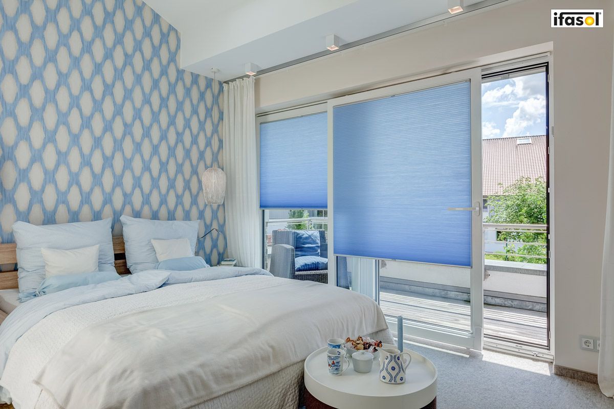 ein Schlafzimmer mit einem Bett , einem Tisch und einer Schiebetür - Sonnenschutz von Gardinen Breuß aus Elmshorn