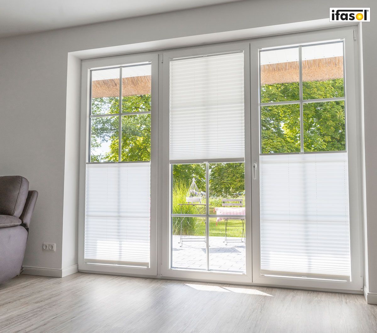 ein Wohnzimmer mit einer Couch und einem großen Fenster mit weißen Jalousien - Sonnenschutz von Gardinen Breuß aus Elmshorn