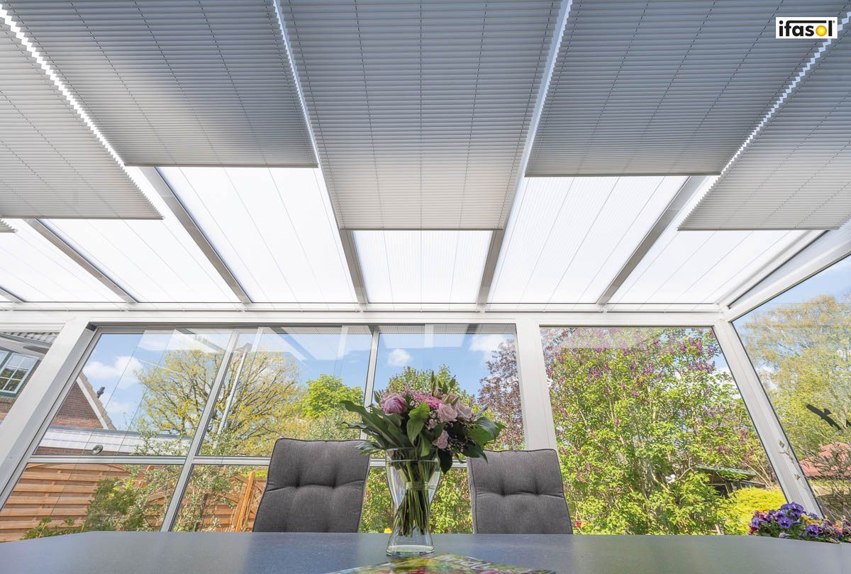 ein Esszimmer mit einem Tisch und Stühlen und einer Vase mit Blumen - Sonnenschutz von Gardinen Breuß aus Elmshorn