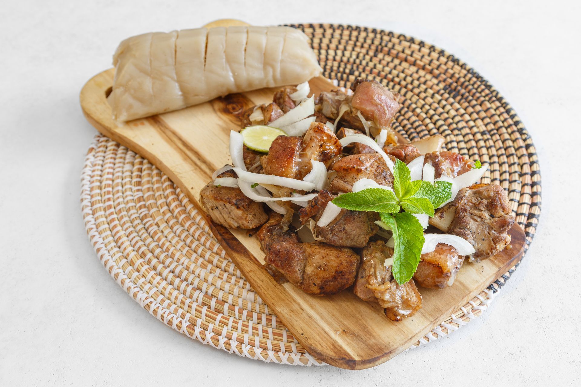 Viande grillée et pain injera sur une planche en bois, garnis d'oignons et d'herbes, le tout posé sur une natte tressée.