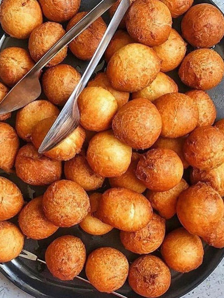 Des boulettes de pâte frites, dorées et rondes, empilées sur un plateau, avec des pinces de service.