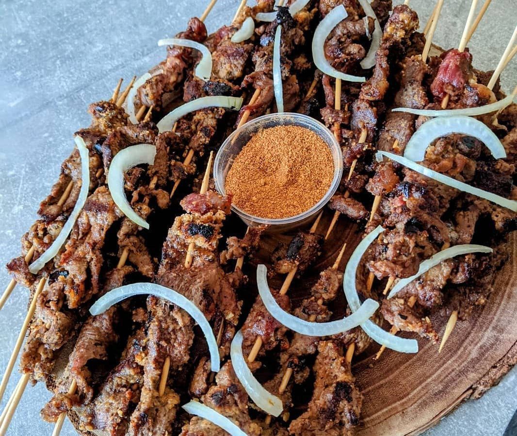 Brochettes de viande grillée avec oignons et bol d'assaisonnement sur une planche en bois.