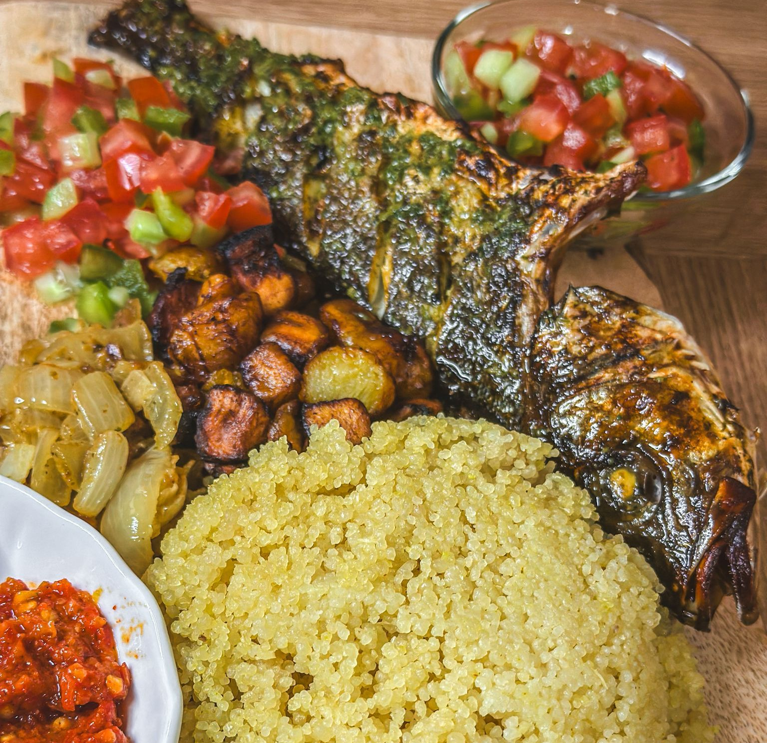 Assiette de poisson grillé avec couscous, légumes rôtis et salade de tomates.