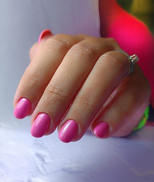 La mano de una mujer con uñas rosas y un anillo en el dedo.