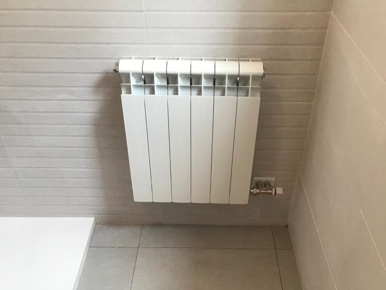 Un radiador blanco está montado en la pared en un baño.
