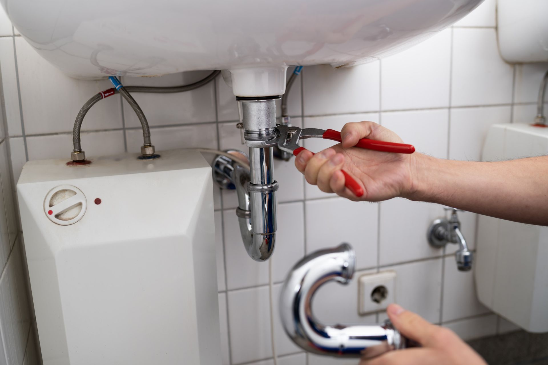 Una persona está arreglando un lavabo en un baño con una llave inglesa.