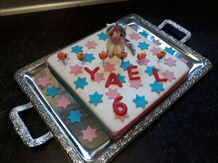Einhorn-Geburtstagstorte mit dem Namen „YAEL“ und der Zahl „6“ auf einem silbernen Tablett, verziert mit Sternen.