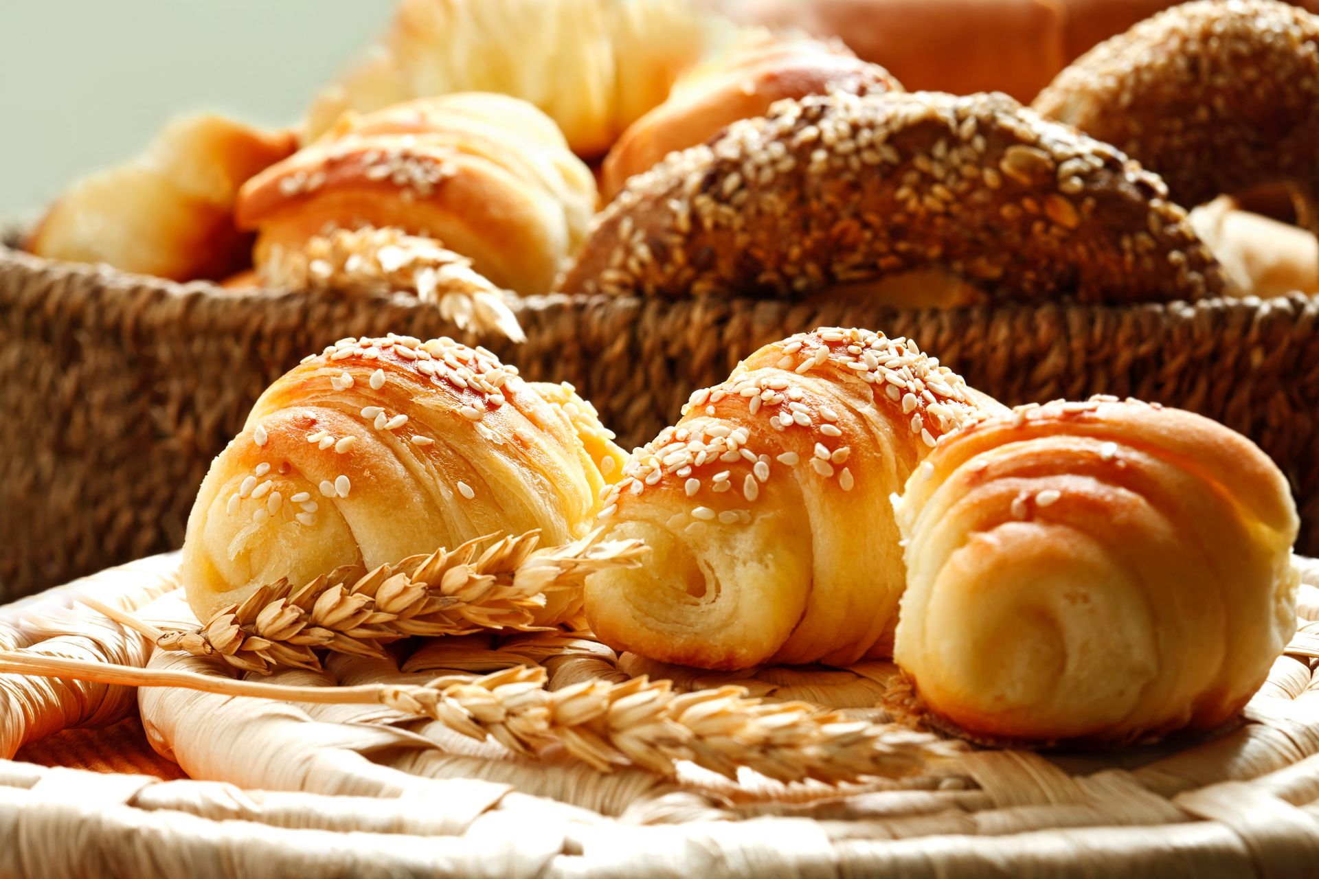 Korb mit verschiedenen Brötchensorten, darunter Croissants, bestreut mit Sesamkörnern.