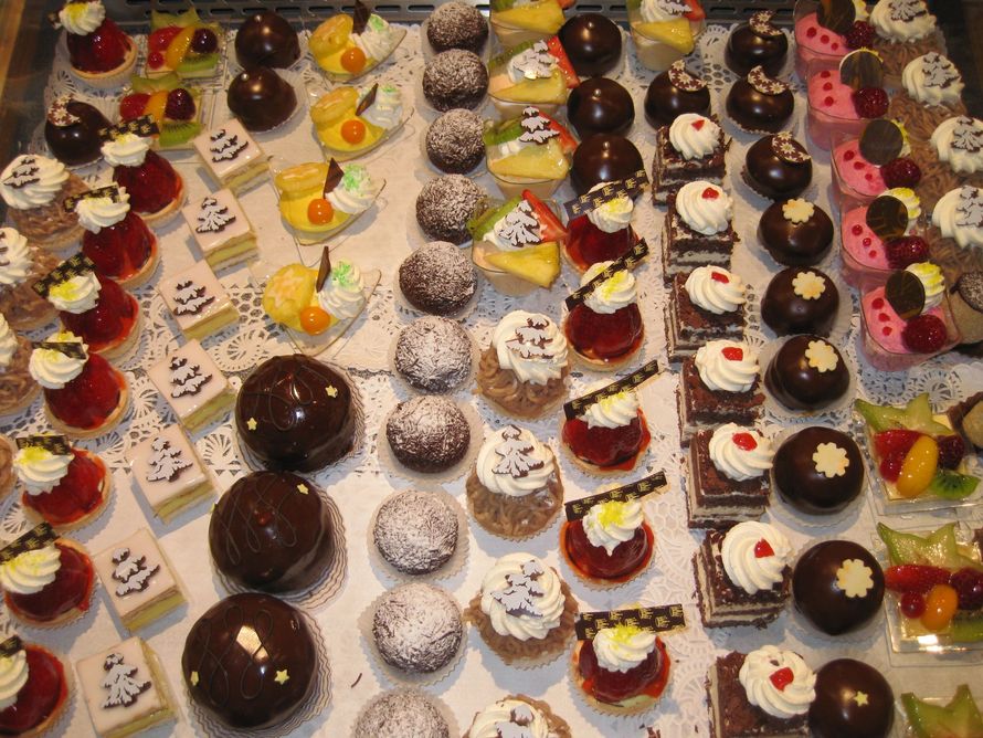 Eine Person in weisser Uniform stellt drei Cupcakes mit rosa Zuckerguss auf eine Theke in einer Bäckerei.
