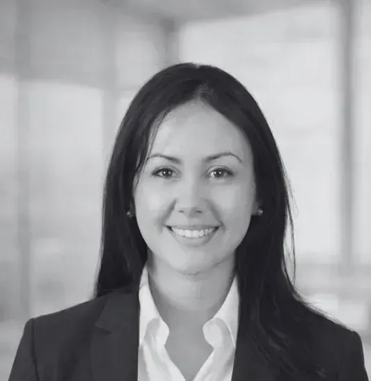 Una mujer con blazer y camisa de cuello blanco sonríe en el interior.