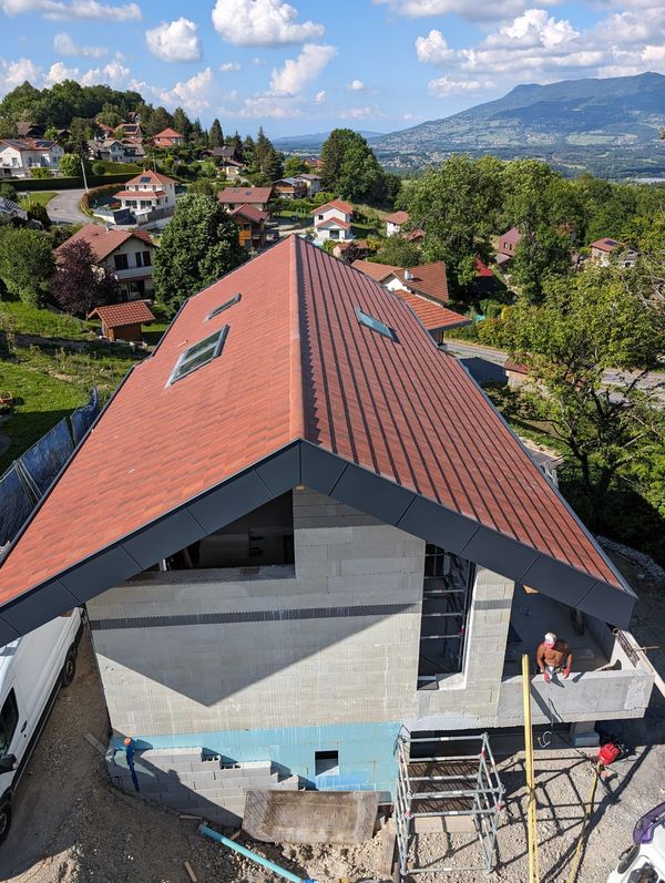 Vue en plongée d'une maison en construction avec un nouveau toit de tuiles, des murs en maçonnerie et un magnifique panorama montagneux.