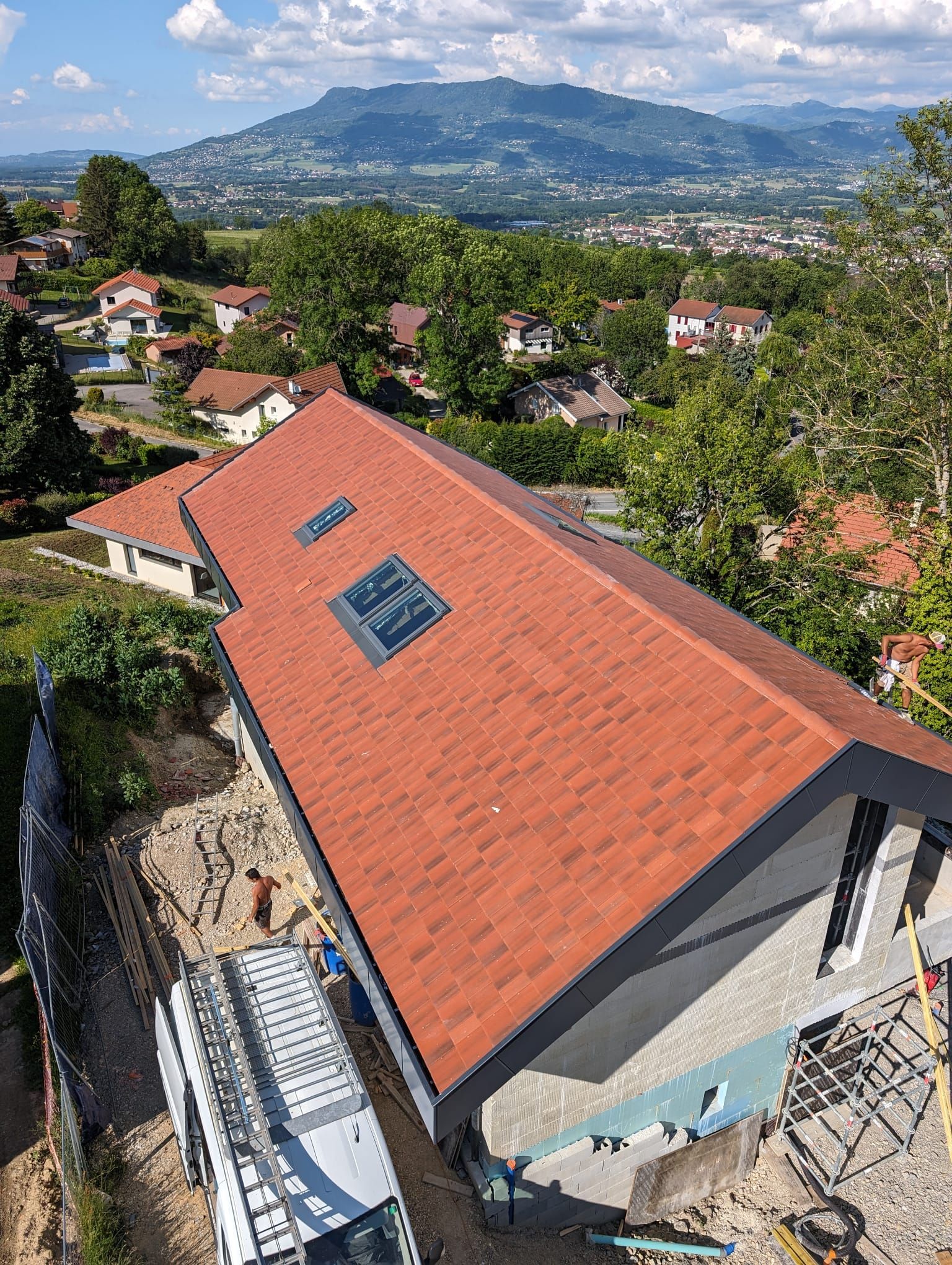 Vue en plongée d'une maison neuve avec un toit de tuiles et des puits de lumière, située dans un quartier avec une vue magnifique sur les montagnes.