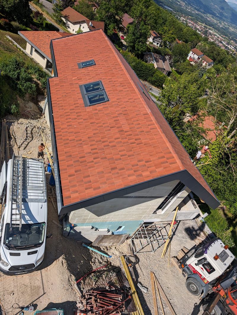 Vue en plongée d'une maison avec un nouveau toit de tuiles, doté de deux puits de lumière, entourée d'engins de chantier.