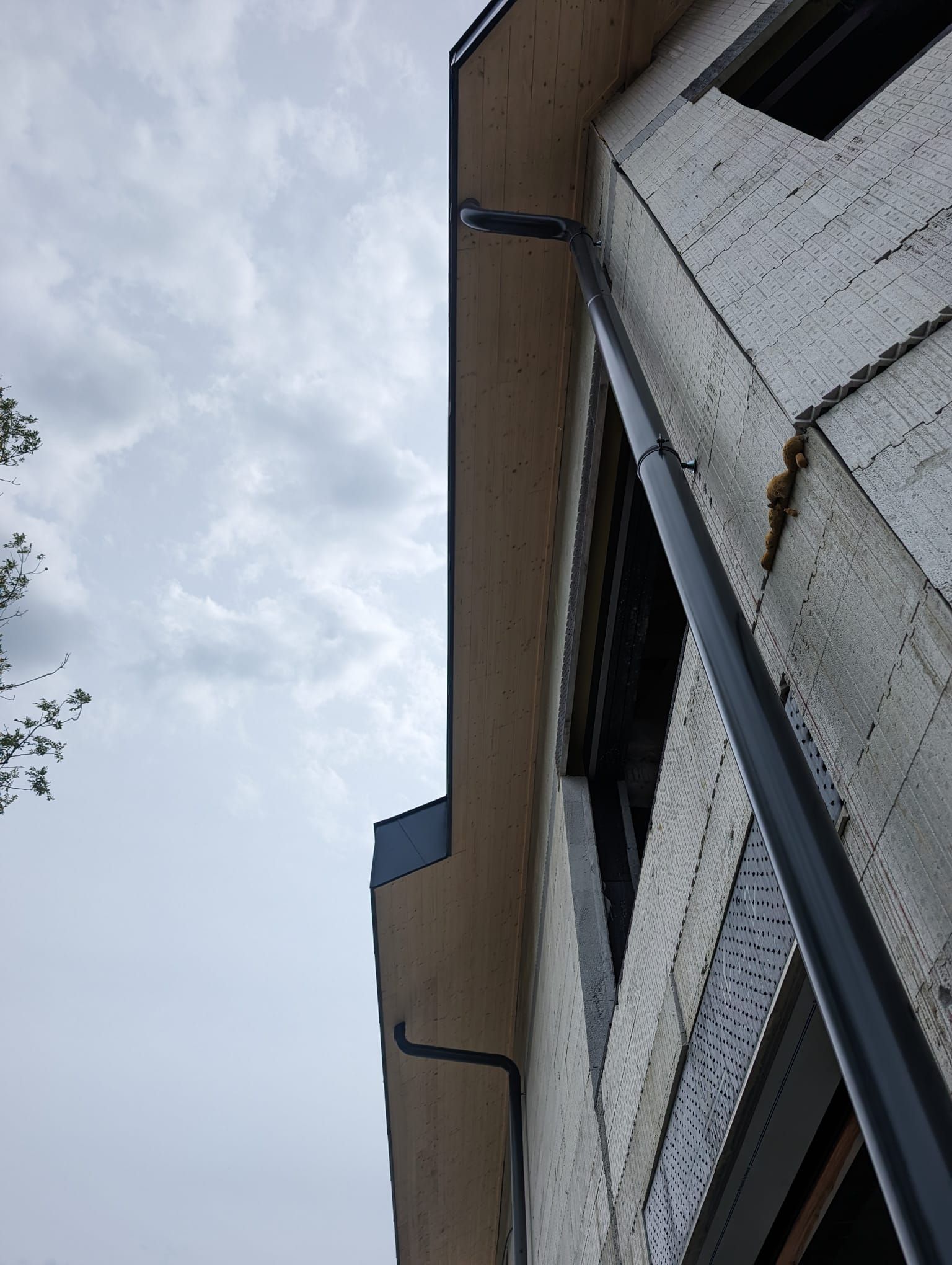 Vue en contre-plongée de descentes de gouttière fixées au mur extérieur inachevé d'un bâtiment.