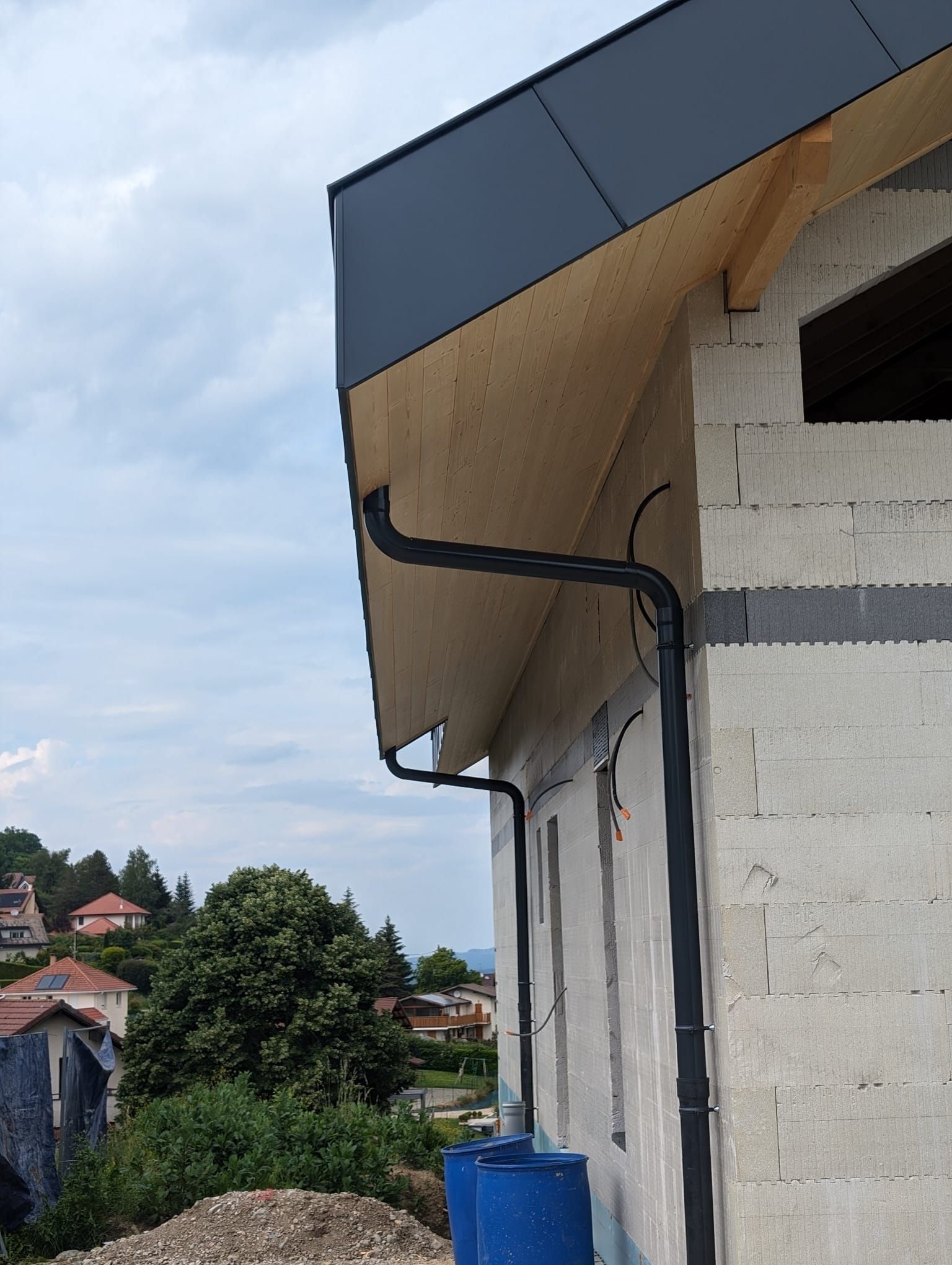 Un système de gouttières installé à l'extérieur d'une maison en blocs de béton inachevée, avec un avant-toit en bois.