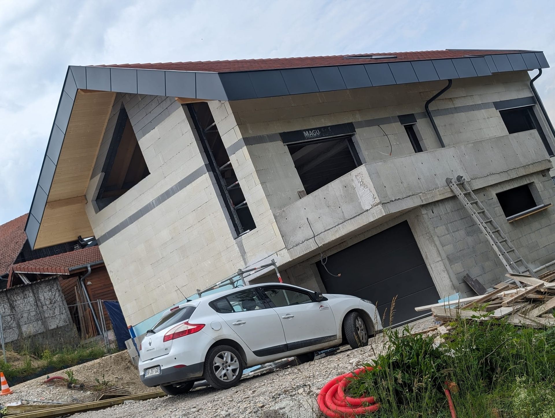 Une voiture à hayon est garée devant une maison moderne de deux étages en construction, avec un toit.
