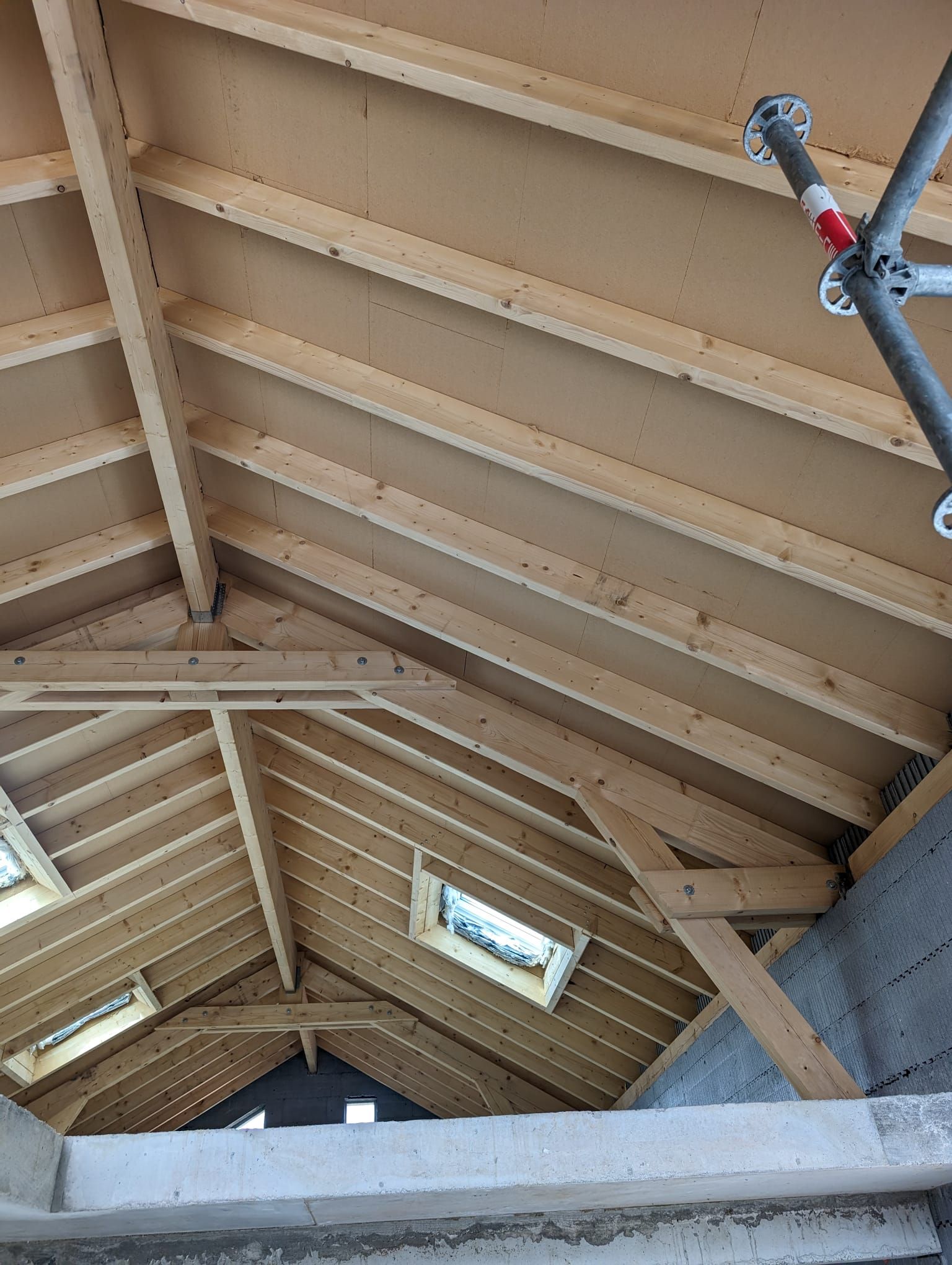Toiture intérieure inachevée avec chevrons apparents, poutres de soutien et deux puits de lumière en construction.