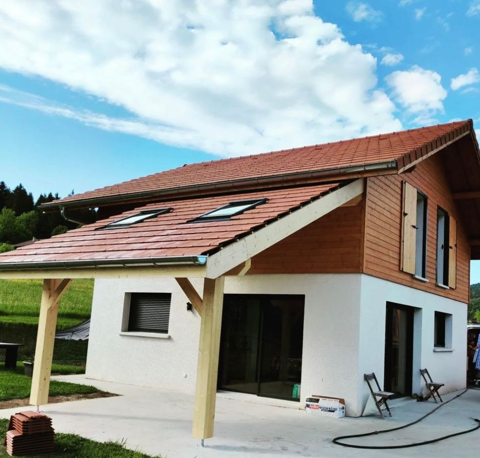 Une maison à deux étages avec des murs, des lambris, un toit de tuiles et une grande terrasse couverte soutenue par des poutres en bois.