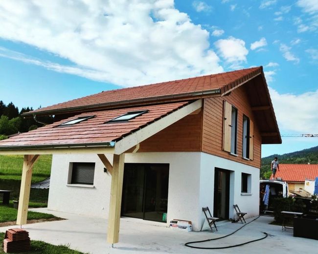 Une maison à deux étages avec un rez-de-chaussée, un étage supérieur en bois et un porche couvert sous un toit de tuiles.