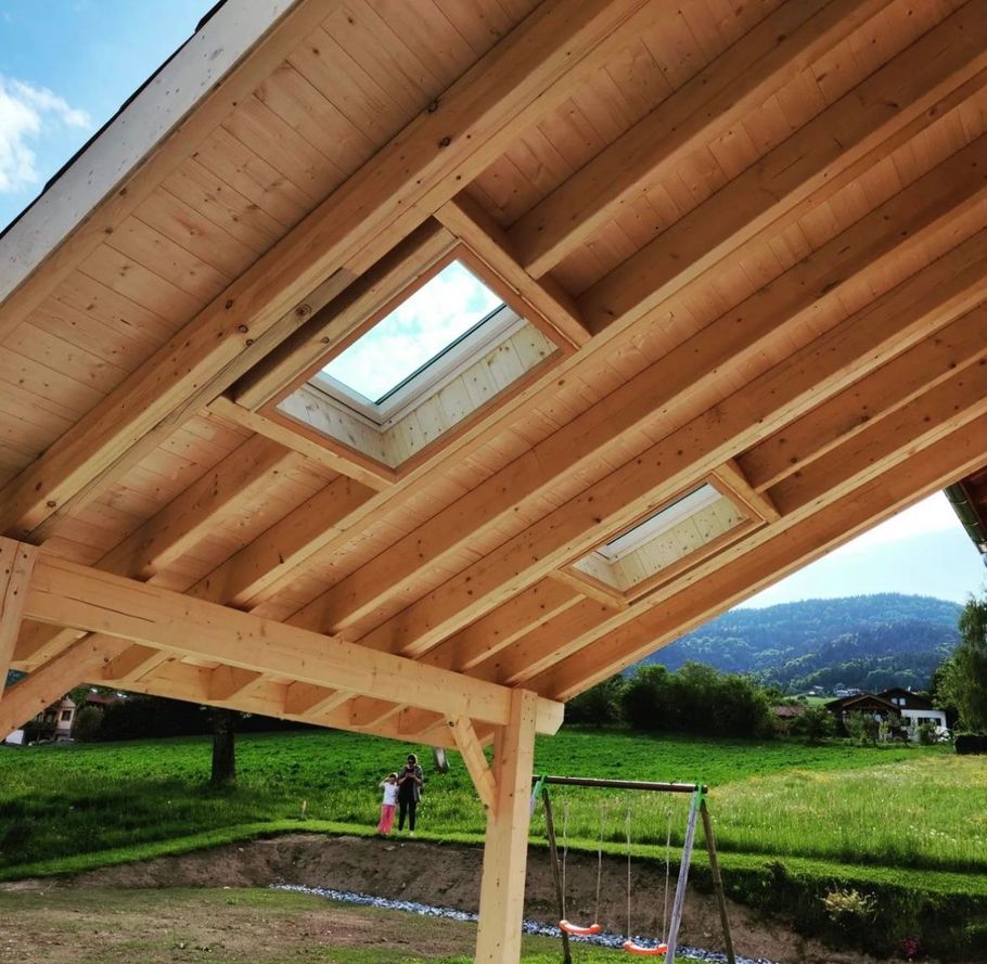 Un toit en pergola avec deux puits de lumière intégrés surplombe une cour gazonnée avec des montagnes en arrière-plan.