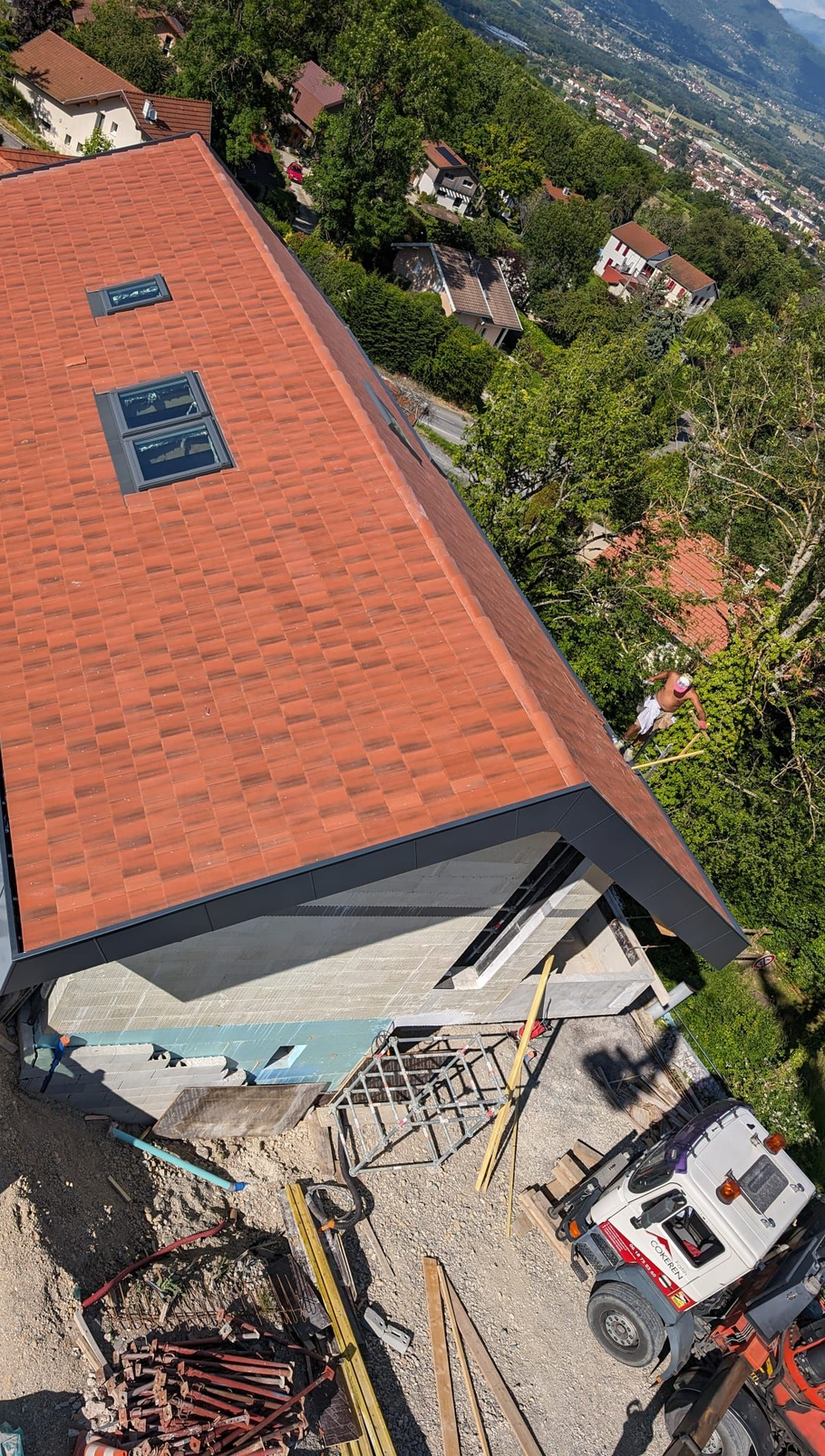 Vue en plongée d'une maison avec un toit en bardeaux récemment installé, une camionnette et des engins de chantier à proximité.