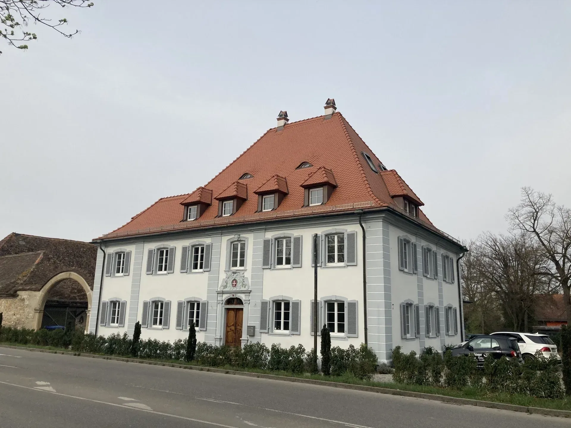 Neben einer Straße steht ein großes weißes Gebäude mit einem roten Ziegeldach.