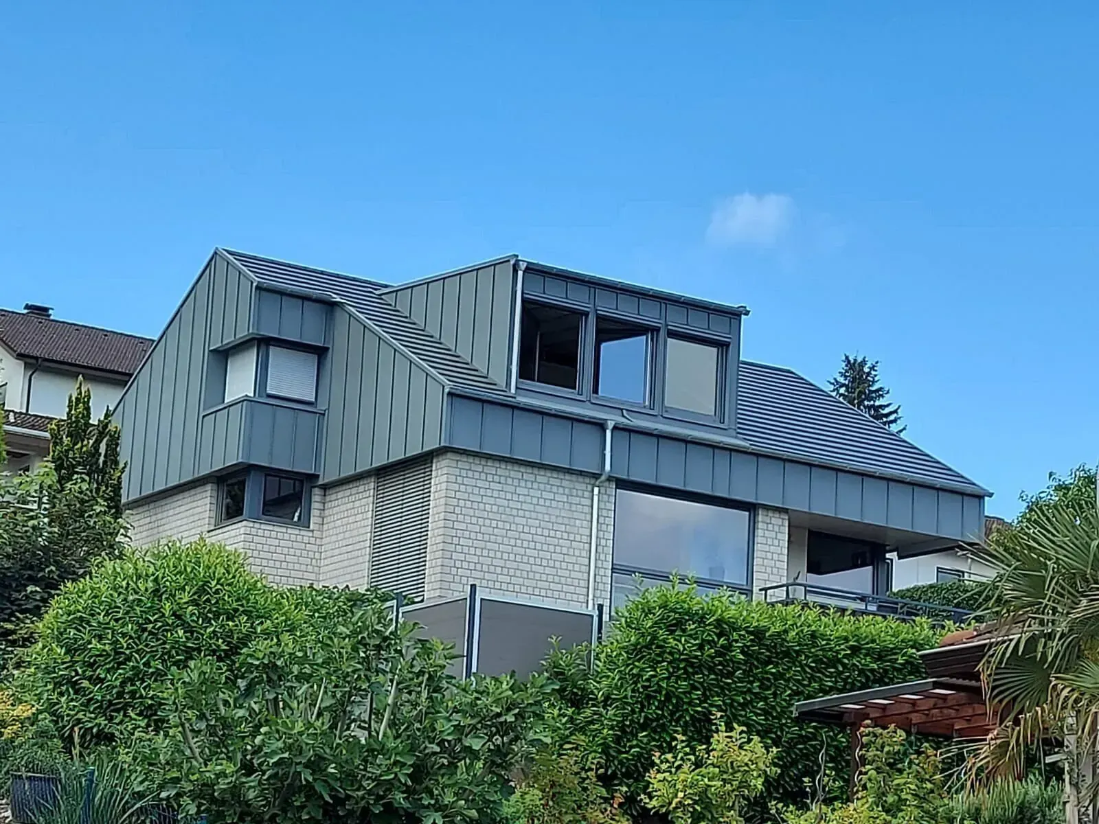 Ein großes Haus mit einem Dach, das von Bäumen und Büschen umgeben ist.