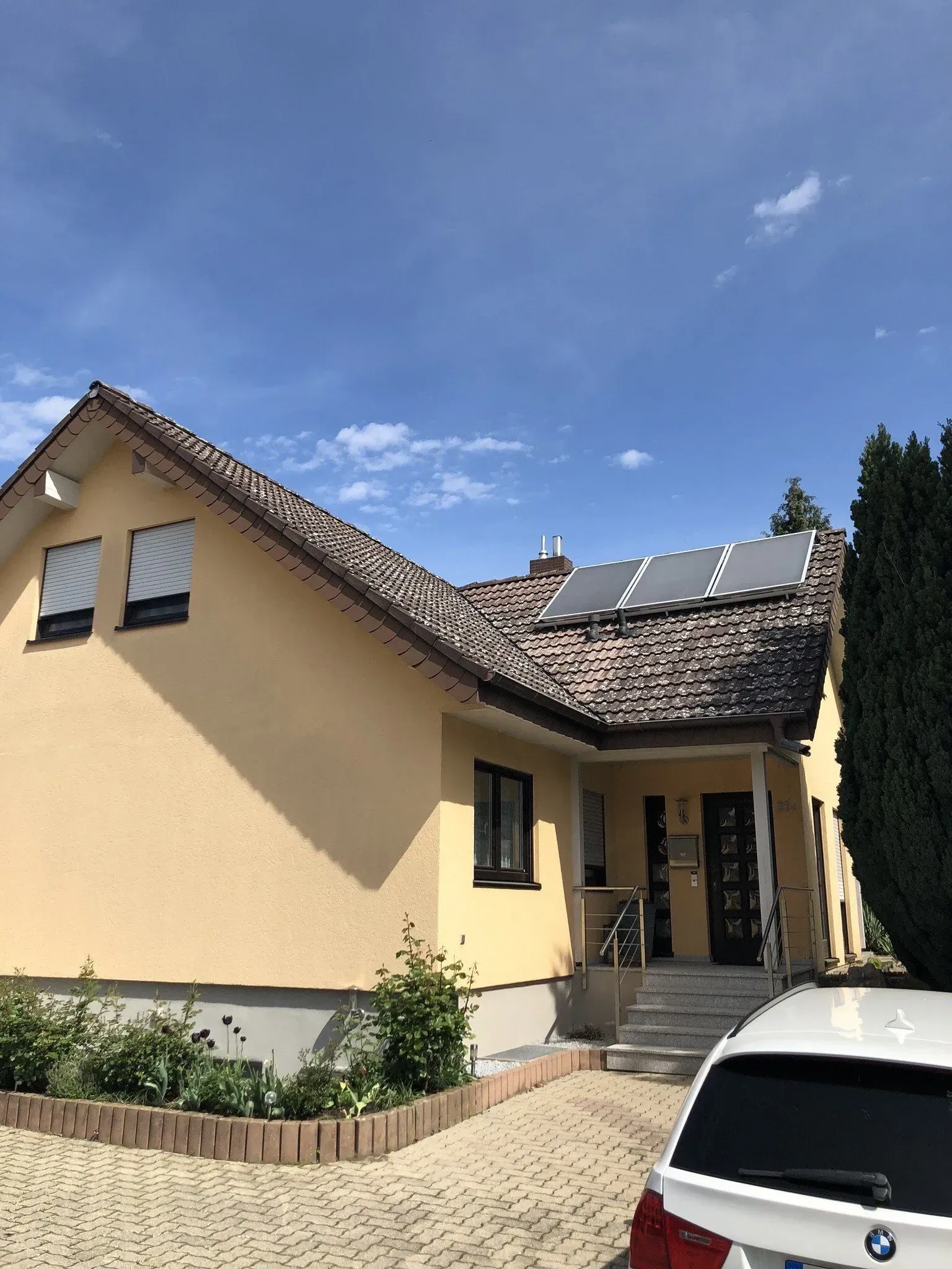 Ein Auto parkt vor einem gelben Haus mit Solarzellen auf dem Dach.