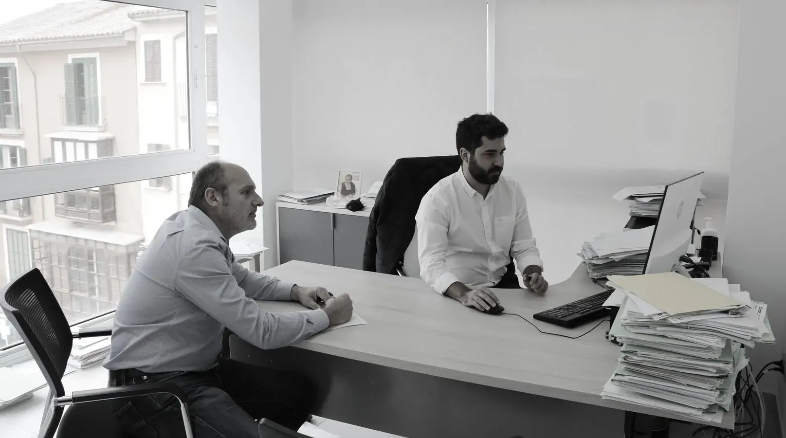 Dos hombres están sentados en un escritorio frente a una computadora.