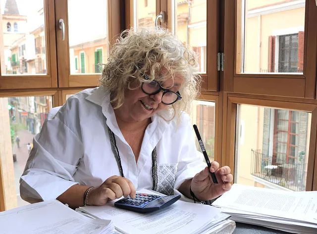 Una mujer está sentada en un escritorio usando una calculadora y un bolígrafo.